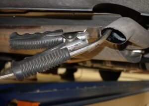 Close-up of a diagnostic tool clamped to a car's exhaust pipe during emission repairs in a workshop